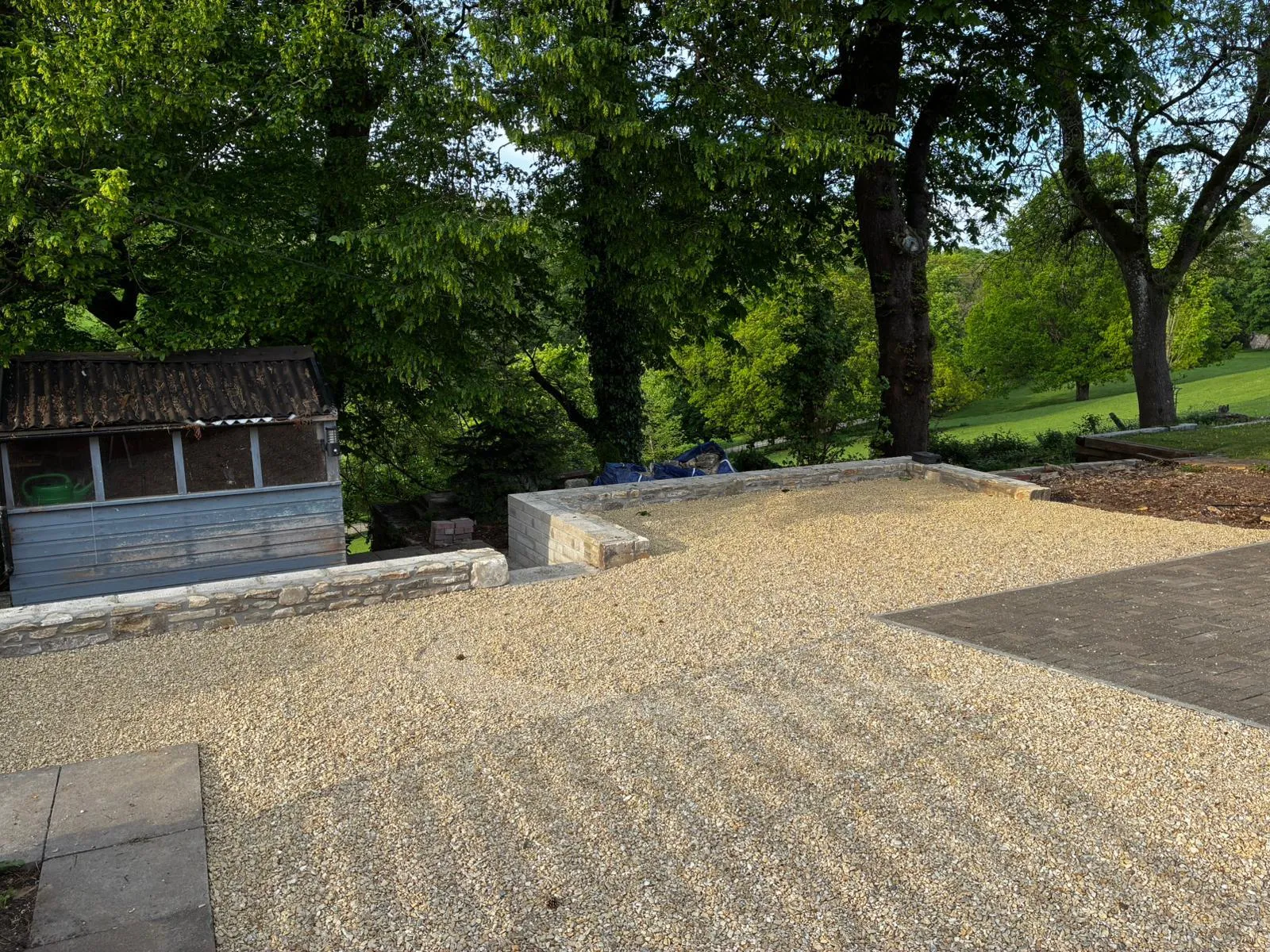 A gravel driveway with stone retaining walls and a shed in the background.