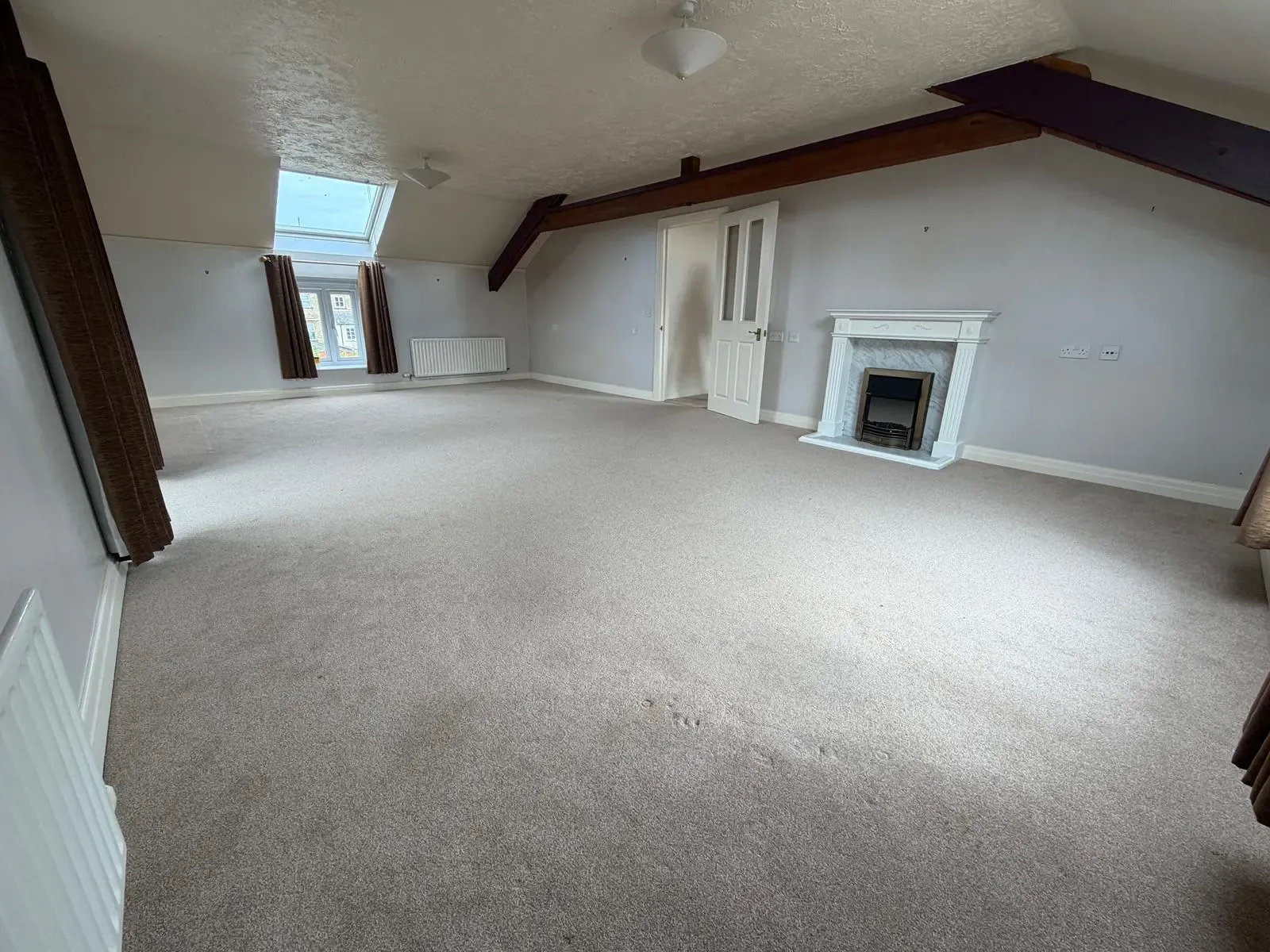 Large empty room with exposed beams and sloping ceiling in a Cotswold property, ready for spatial reconfiguration or bespoke joinery fit-out by Fortura Construction LTD.